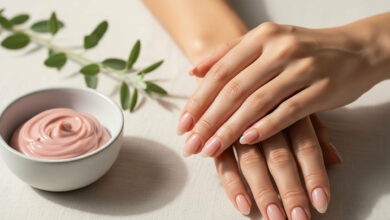The ultimate guide to youthful hands and strong, healthy nails, featuring a close-up of a woman's beautifully manicured hands next to a bowl of dusty rose hand cream and a green sprig.