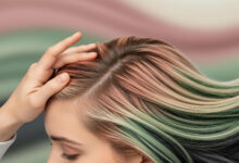 A close-up, photorealistic image focusing on a person's healthy scalp and multicolored hair. The hair is styled with streaks of dusty rose, sage green, cream, and charcoal. One hand gently runs through the hair at the crown of the head, while the other holds the ends. The background is a soft, blurred composition of the same colors, creating a serene atmosphere.