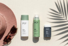 A guide to choosing and applying sunscreen correctly, shown as a flat-lay with a sun hat, sunglasses, and various sunscreen types (lotion, spray, stick) on a cream surface with a palm leaf shadow.
