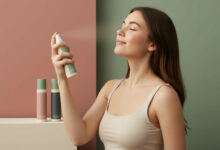 A smiling woman with her eyes closed sprays a hydrating mist onto her face, enjoying the refreshing sensation for tired skin.