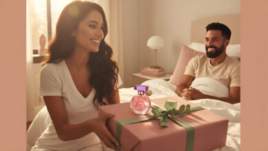 A gorgeous woman smiling as she presents a beautifully wrapped gift box with a celebrity fragrance (like Ariana Grande's) to a happy man in bed, addressing if such perfumes make good gifts.