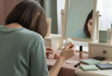 A woman at a vanity table looks down at an oil-blotting paper, reviewing its effect on her foundation base.