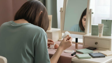 A woman at a vanity table looks down at an oil-blotting paper, reviewing its effect on her foundation base.
