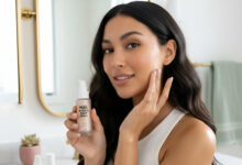 A gorgeous woman with flawless skin holds up Milk Makeup's Hydro Grip Primer in a bright bathroom, demonstrating its application and effectiveness.