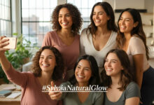 A gorgeous woman with a natural, glowing no-makeup look takes a selfie in a sunlit bedroom for the #SylvaiaNaturalGlow Challenge.