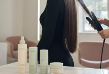 A woman in a salon gets her long, sleek hair straightened with a flat iron, showcasing the best products for achieving the "Glass Hair" trend.