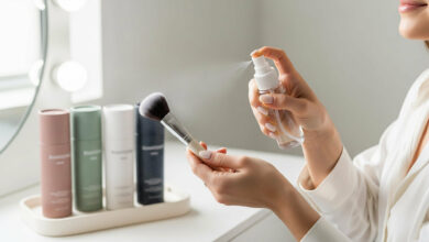 Woman cleaning a makeup brush with sanitizing spray, with various colorful bottles on a vanity, for a review of the best brush cleaners.