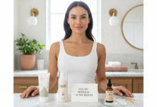 A gorgeous woman in a clean bathroom stands behind a display of three "clean beauty" mineral sunscreen brands, comparing their formulations.
