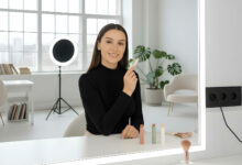 A confident woman applies contour makeup in a bright, modern room, as if filming a tutorial.