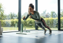 A dynamic woman performs a high-intensity exercise in a bright, modern home gym with expansive windows.