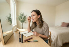 a woman at a sunlit vanity testing multiple volumizing mascaras on her sparse lashes, comparing the results for a fuller look.