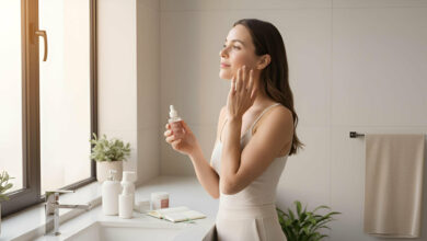 A serene woman in her late 20s, Mia, applies serum to her clear, radiant skin in a bright, modern bathroom. Minimalist products and soft natural light create a calm atmosphere, suggesting confidence gained from a consistent self-care routine.