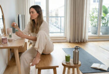 a woman in a sunlit room managing hormonal acne, demonstrating a comparison between applying topical skincare products and adopting lifestyle changes like yoga and healthy hydration.
