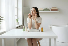 A serene woman applies serum to her clear skin in a bright, modern bathroom.