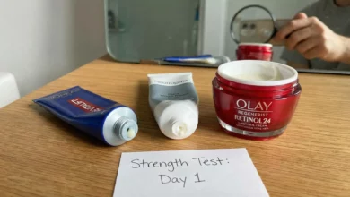 A photorealistic flat lay comparing L'Oréal, Neutrogena, and Olay retinol containers arranged on a sunlit wooden table with sage green accents