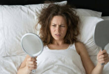 A frustrated woman looking at her messy, frizzy hair in a mirror after waking up