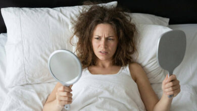A frustrated woman looking at her messy, frizzy hair in a mirror after waking up