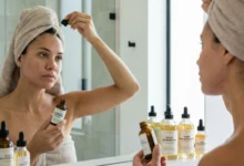 A candid photograph of a woman with a towel on her head applying a probiotic serum. Several bottles labeled "Scalp Microbiome" and "Hair Skin-ification" are on the bathroom counter, illustrating the 2026 beauty trend of treating the scalp with skincare-grade ingredients.